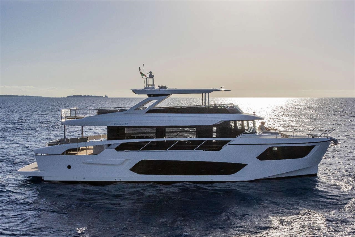 A sleek white luxury yacht sails on the shimmering ocean under a bright sky, with a person at the helm.
